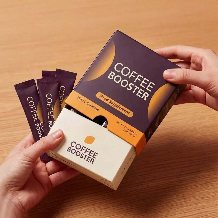 Coffee Booster box opened between two hands, plum packets on a wooden table